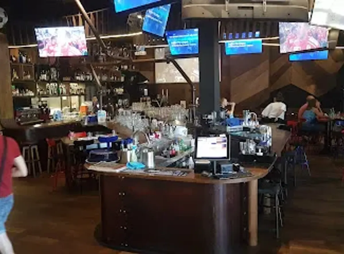 Bar intérieur de The Game avec comptoir circulaire et 40+ écrans de sport