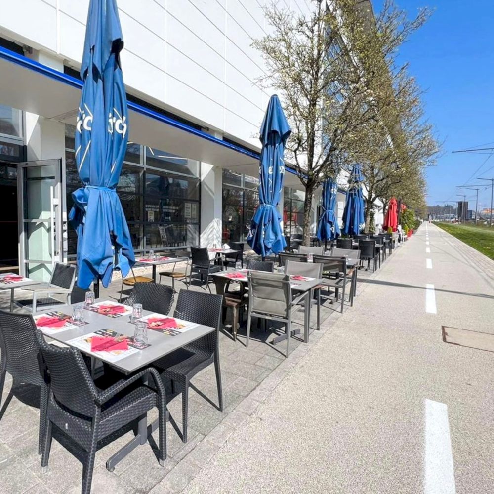 Terrasse extérieure de The Game — rangée de tables avec parasols bleus